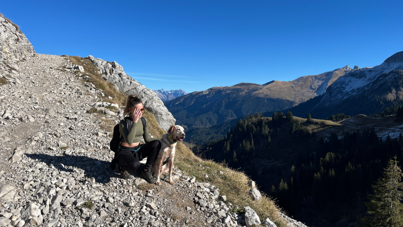 Femme en randonnée avec son chien équipé d’un harnais OrkaDog, assise face à un panorama de montagne